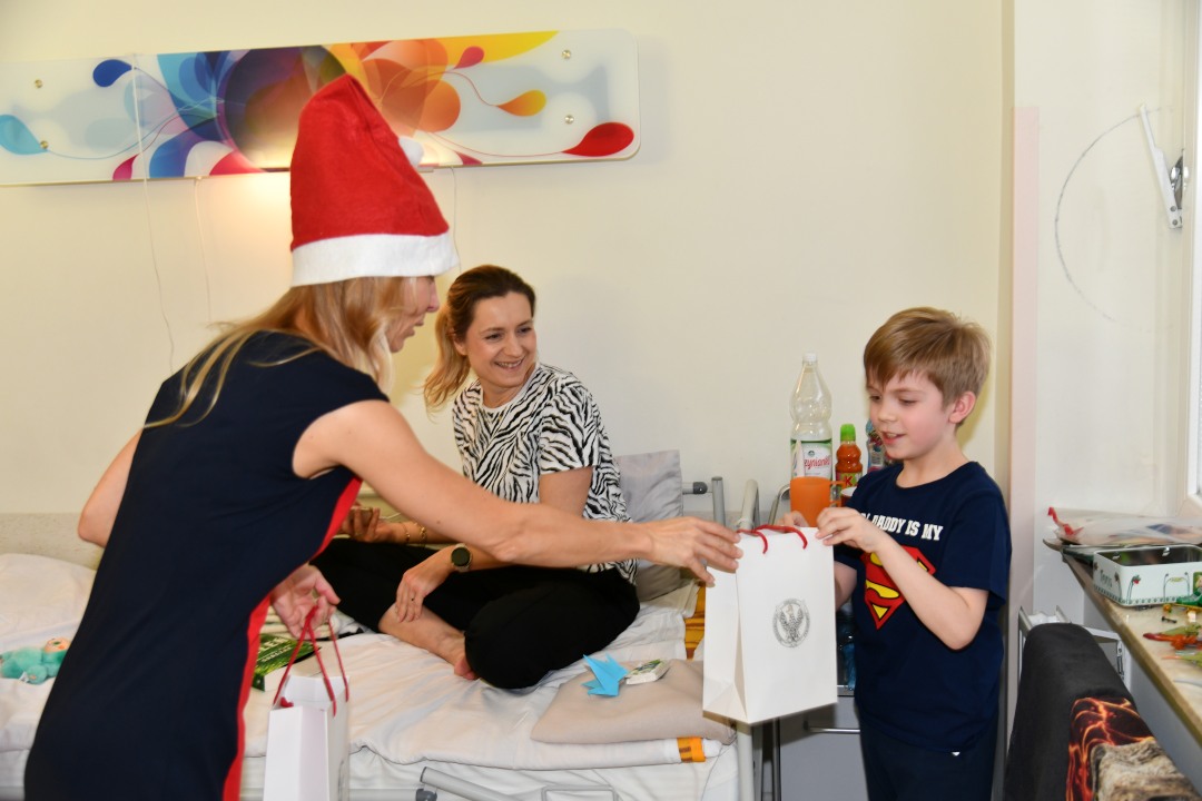 Małgorzata Złotkowska w czapce świętego Mikołaja wręcza prezent chłopcu.