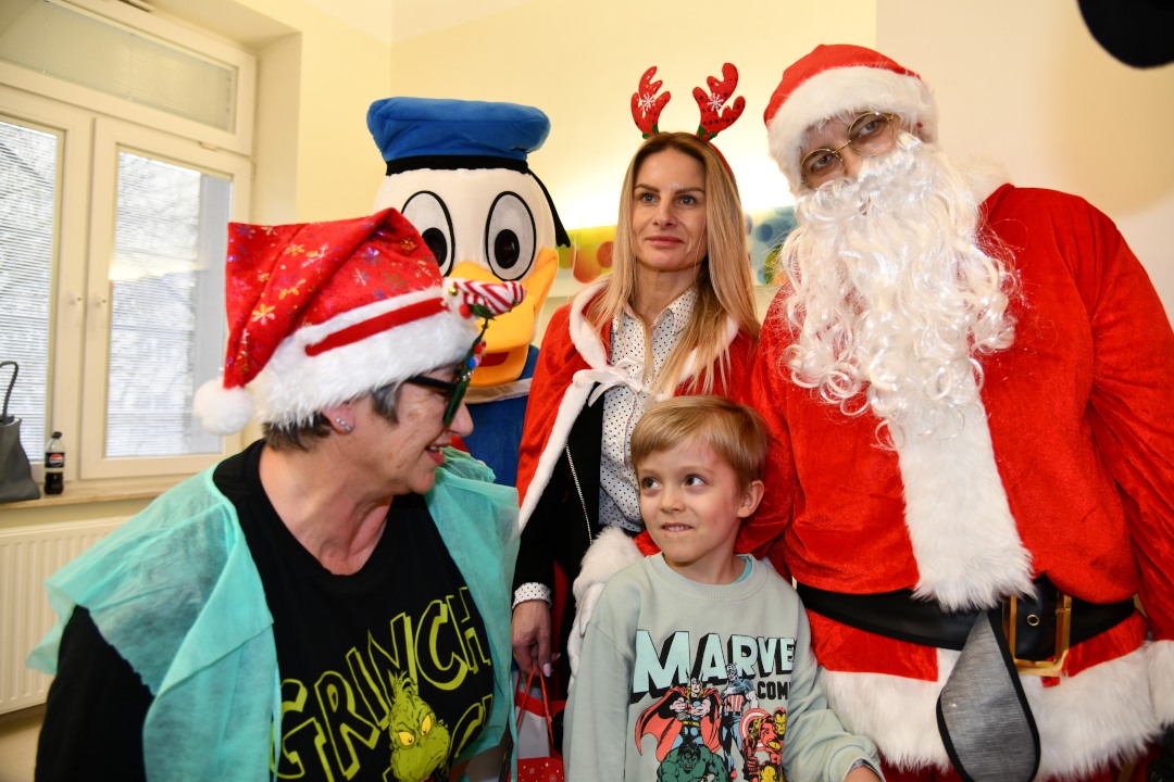 Mały pacjent z Mikołajem i jego pomocnikami pozują do zdjęcia na sali szpitalnej.