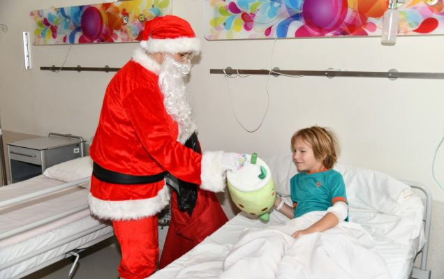 Sala szpitalna. Święty Mikołaj przy łóżku wręcza prezent młodemu pacjentowi.