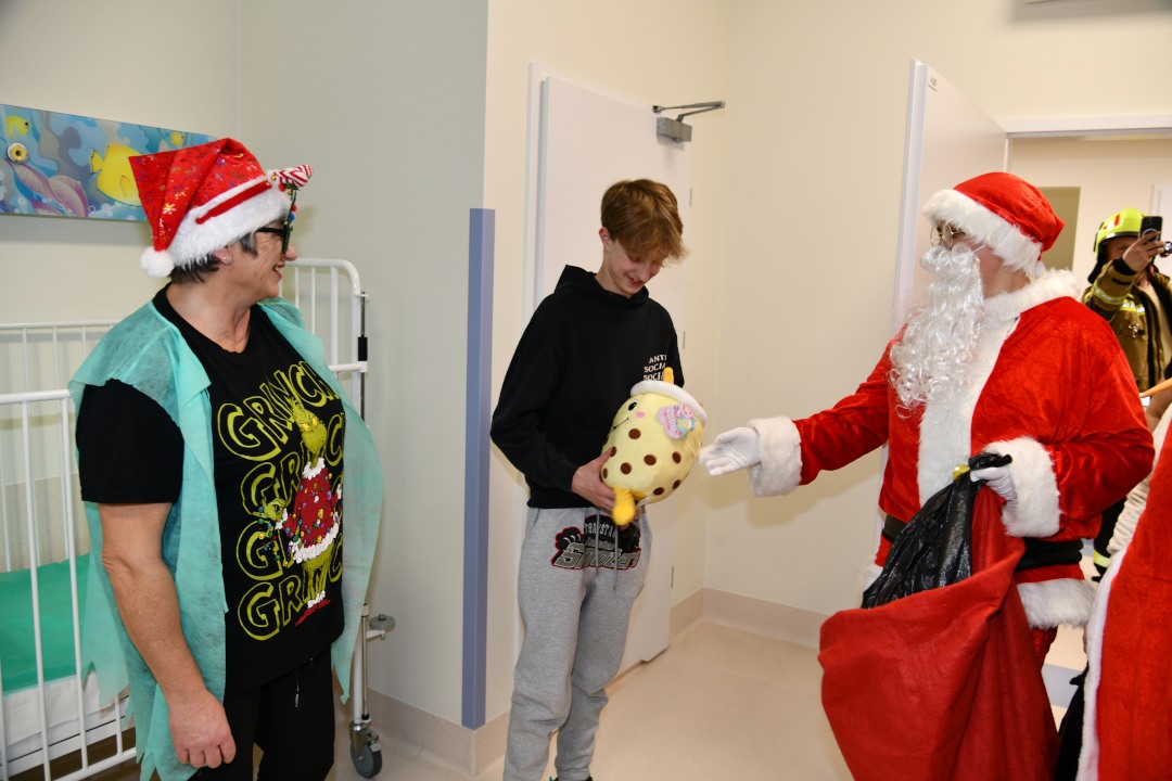 Sala szpitalna. Kubuś Puchatek wręcza prezent nastoletniemu pacjentowi.