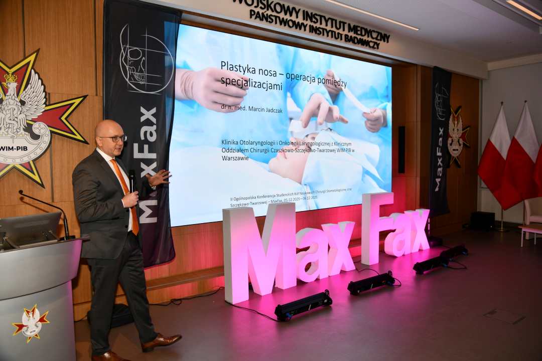 Prelegent podczas konferencji, obok stojący napis Max Fax i ekran ze slajdem z konferencji.