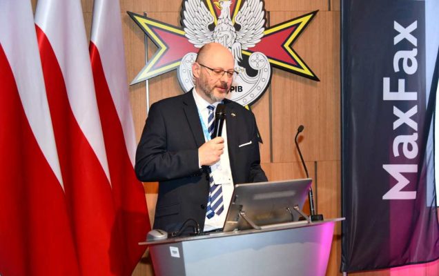 Prelegent przy mównicy. Za nim logo WIM, obok napis MAX FAX.