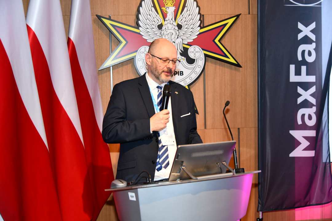 Prelegent przy mównicy. Za nim logo WIM, obok napis MAX FAX.