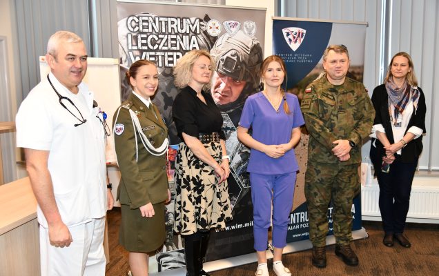 Pracownicy WIM pozują do zdjęcia na tle grafiki reklamowej Centrum Leczenia Weterana.