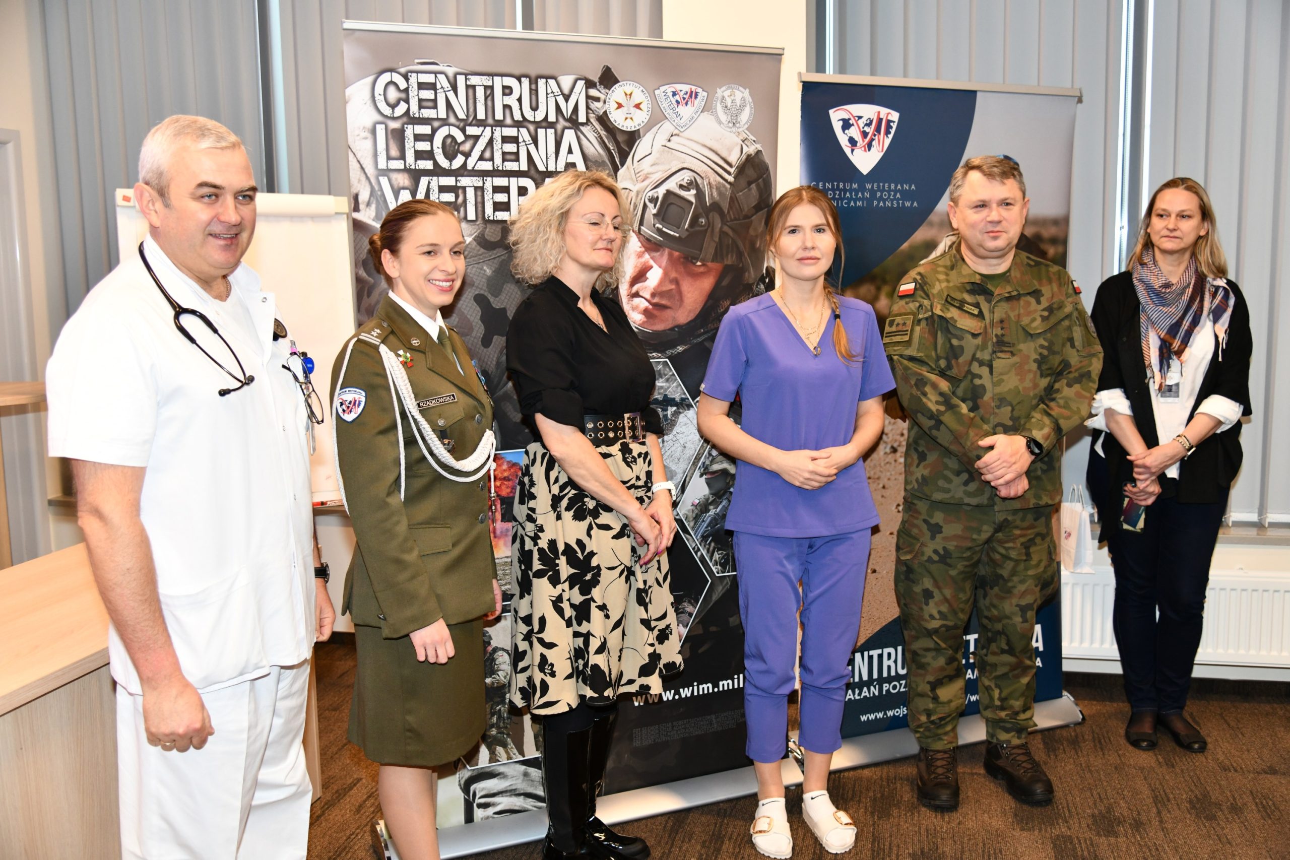 Pracownicy WIM pozują do zdjęcia na tle grafiki reklamowej Centrum Leczenia Weterana.