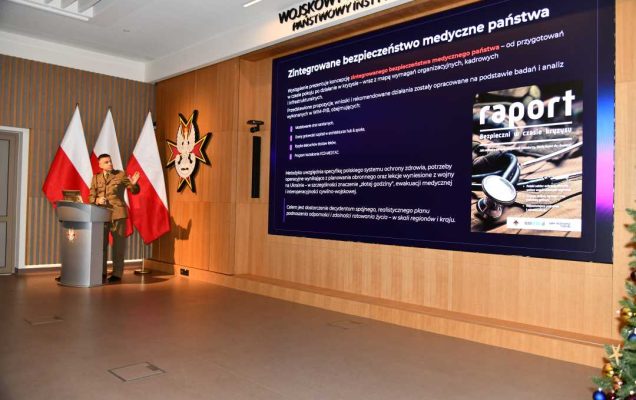 Jarosław Kowal przy mównicy podczas wykładu . Za nim na ekranie plansza tytułowa panelu.