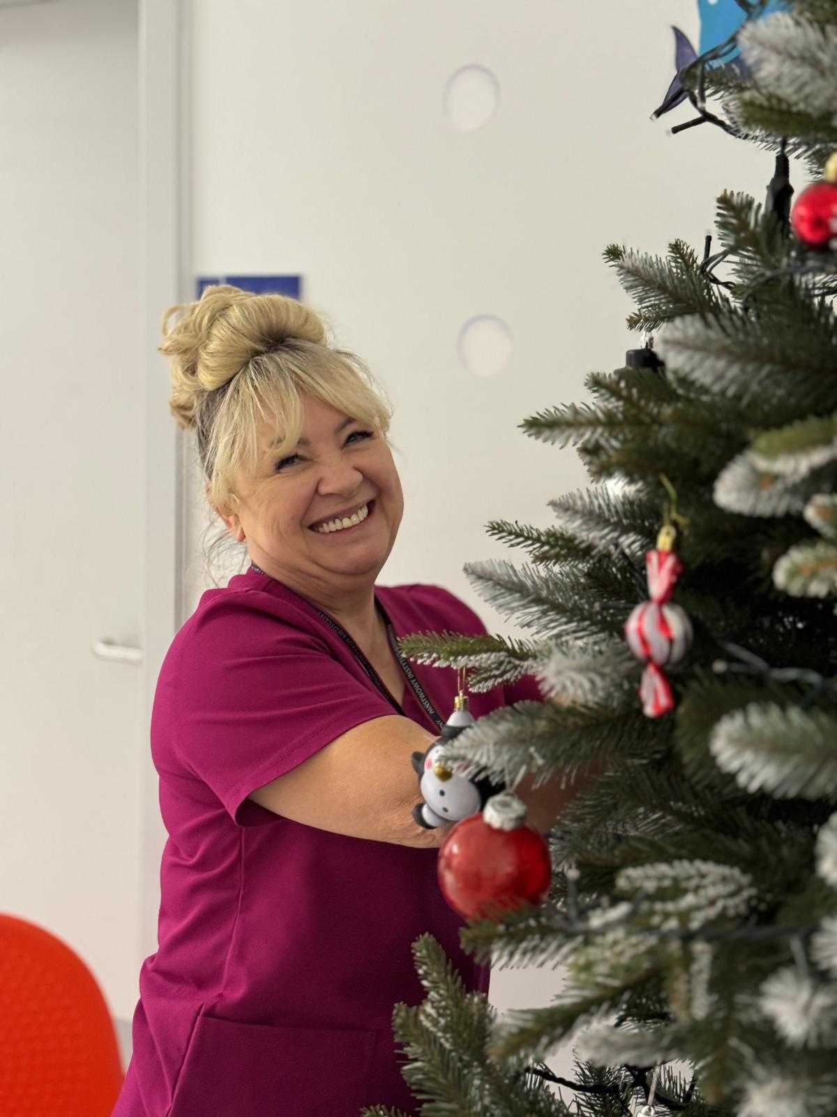 Uśmiechnięta pracowniczka wiesza ozdoby na choince.