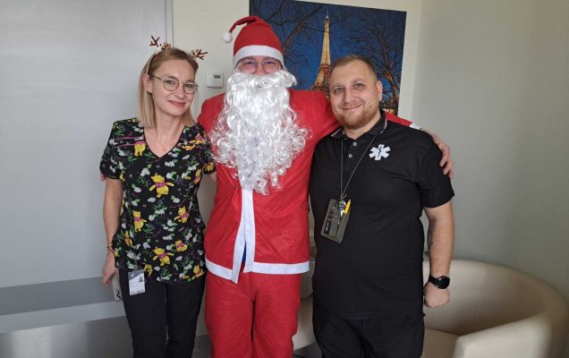 Święty Mikołaj pozuje do zdjęcia z dwoma pracownikami.