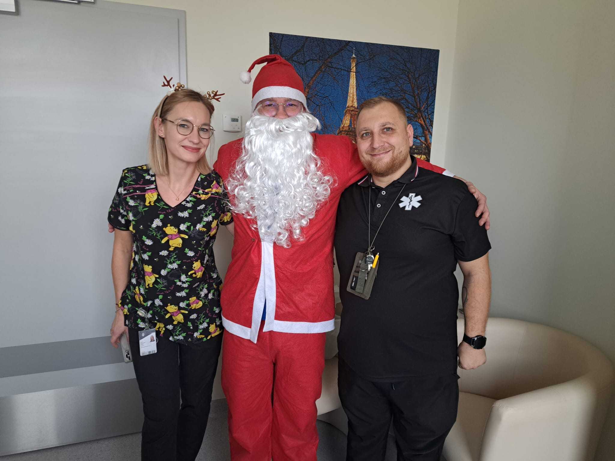 Święty Mikołaj pozuje do zdjęcia z dwoma pracownikami.