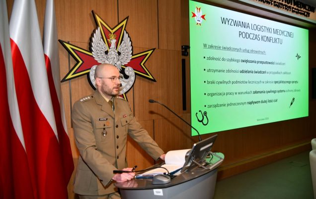 mgr Bartłomiej Kwapisz przy mównicy, za nim na ekranie wyświetlona prezentacja.