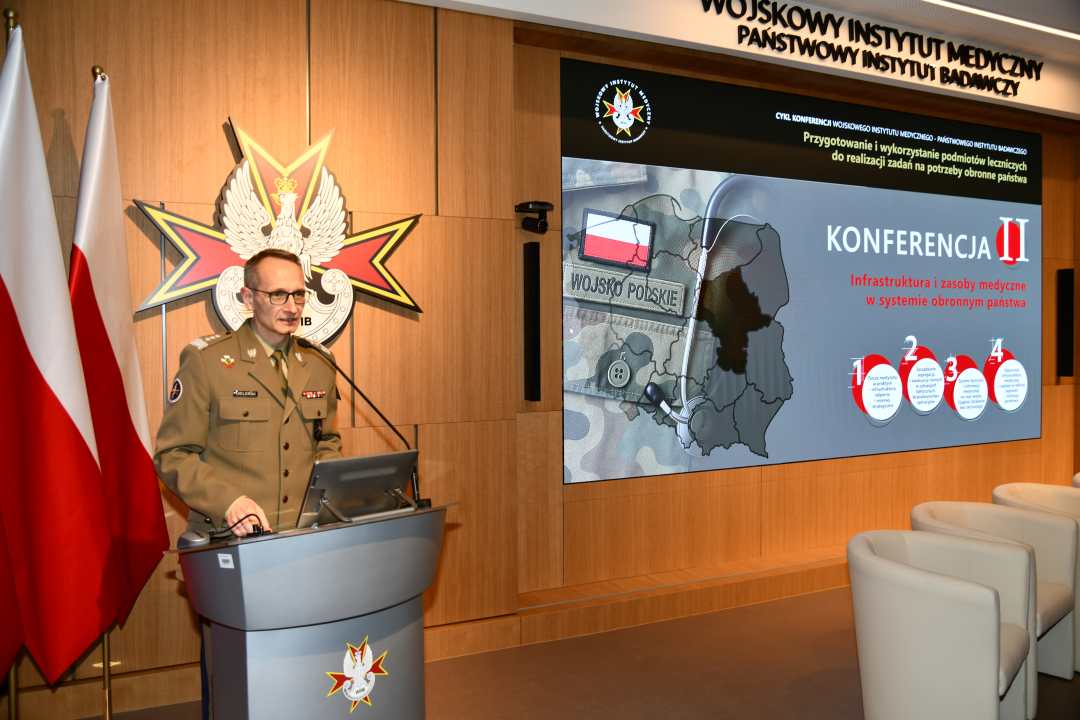 Grzegorz Gielerak przy mównicy, za jego plecami na ekranie prezentacja konferencyjna.