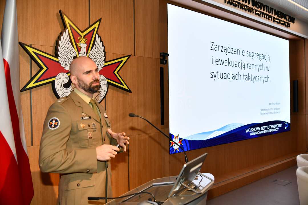 por. mgr Artur Skobel przy mównicy. Za jego plecami na ekranie slajd z konferencji.