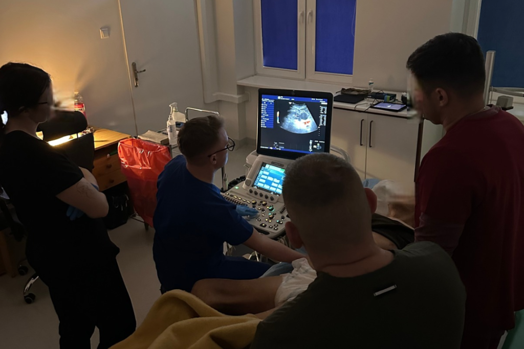 Pacjent i czterech lekarzy podczas badania USG w sali szpitalnej.