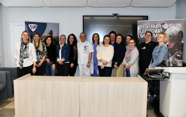 Pracownicy Centrum Leczenia Weterana w sali wykładowej pozują do wspólnego zdjęcia.