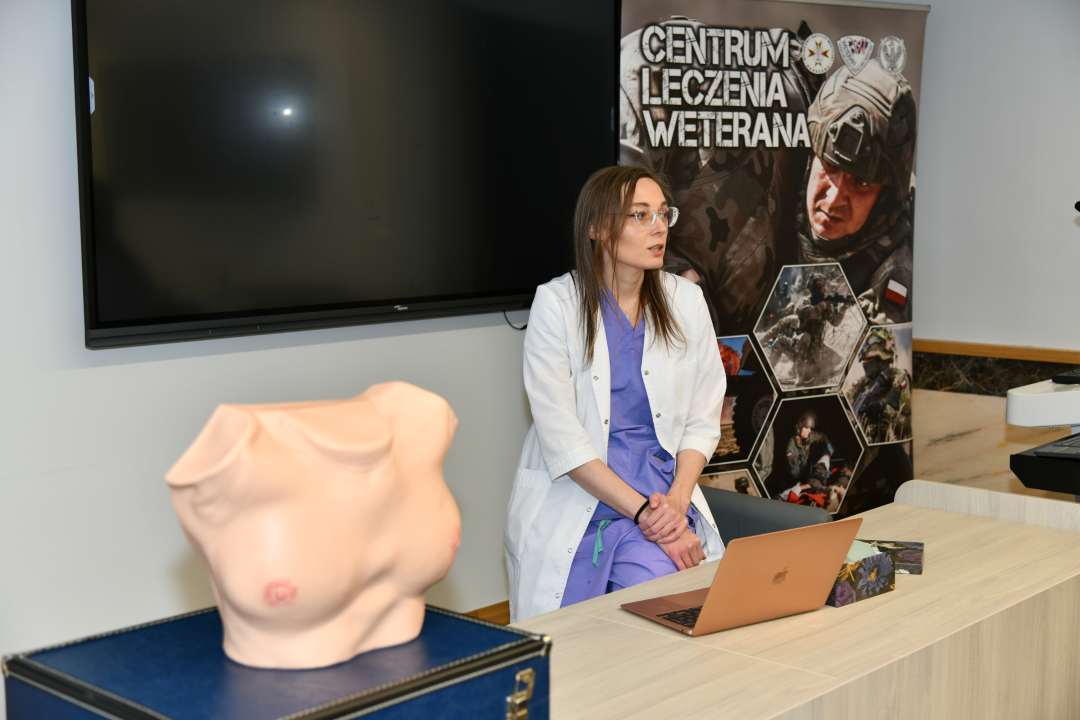 Sala wykładowa. Lekarka prowadząca prelekcję obok niej na katedrze stoi fantom kobiecej klatki piersiowej.