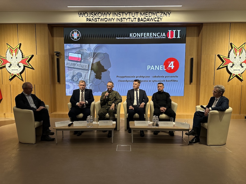 Paneliści siedzący w fotelach. Za nimi ogromny ekran z planszą konferencji.