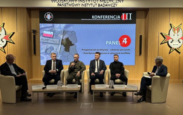 Paneliści siedzący w fotelach. Za nimi ogromny ekran z planszą konferencji.