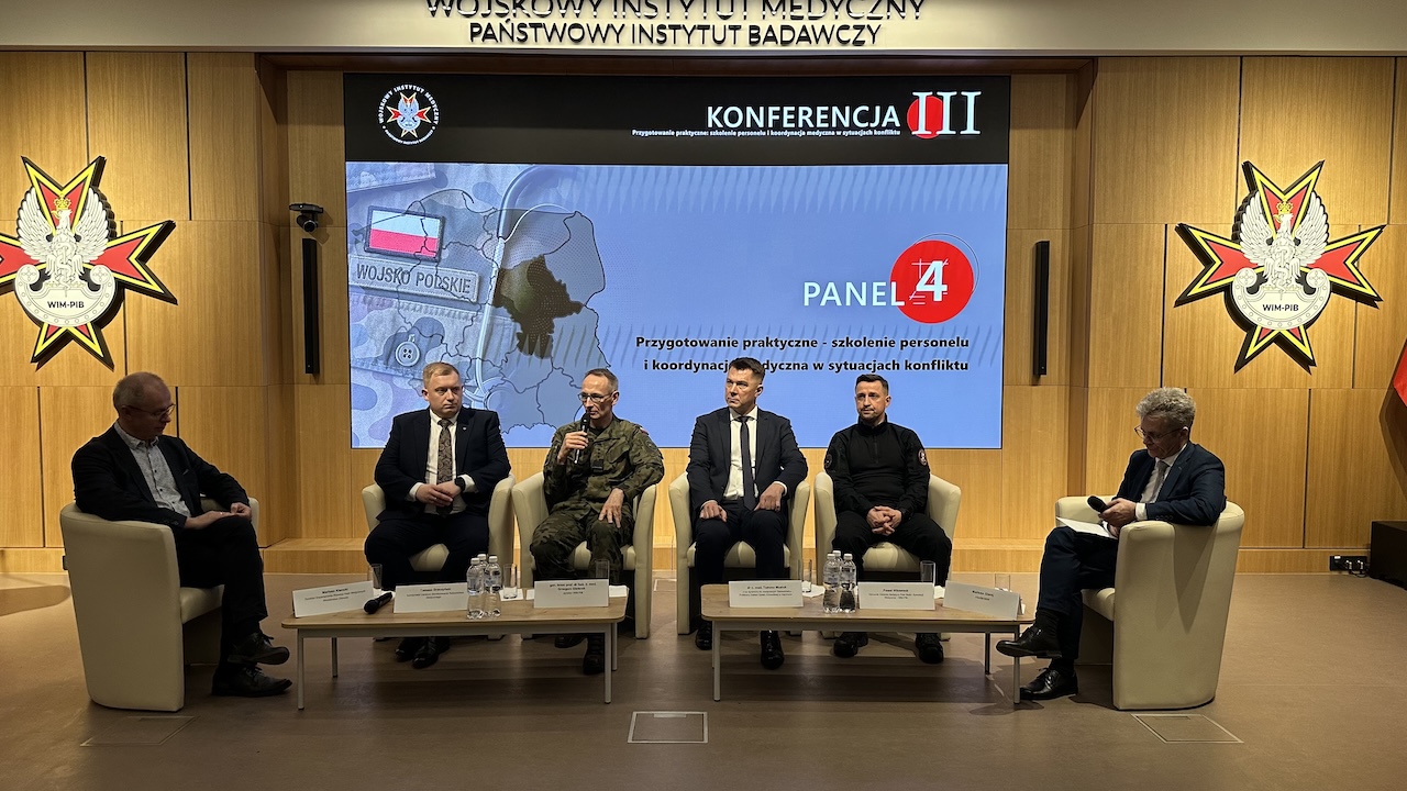 Paneliści siedzący w fotelach. Za nimi ogromny ekran z planszą konferencji.