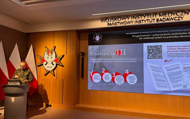 Grzegorz Gielerak przy mównicy za nim na ekranie slajd z konferencji.