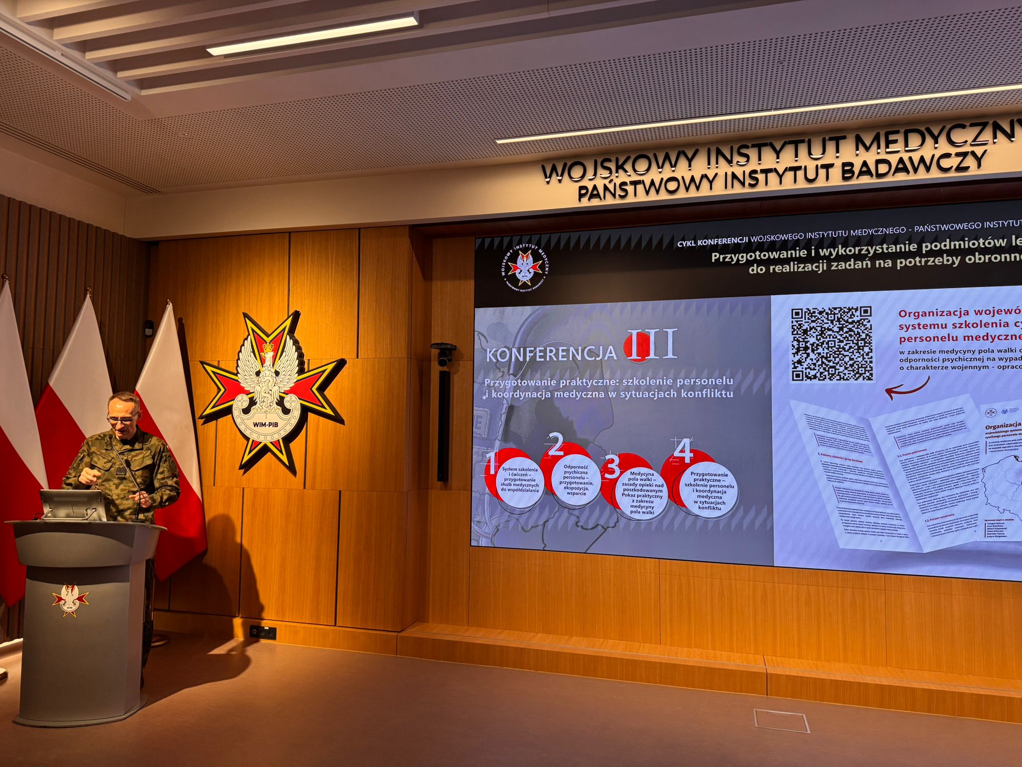 Grzegorz Gielerak przy mównicy za nim na ekranie slajd z konferencji.