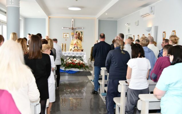 Msza święta. Ujęcie z tyłu kaplicy na ludzi w ławkach i ołtarz.