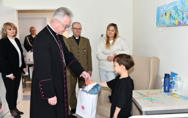 Biskup, dyrektor WIM oraz pracownicy szpitala z wizytą na sali chorych w Klinice pediatrii. Biskup wręcza torbę z prezentem chłopcu.