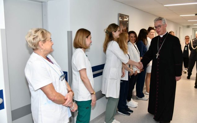 Biskup na korytarzu szpitalnym wita się z pracowniczkami WIM.
