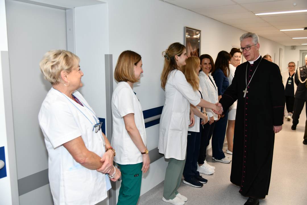 Biskup na korytarzu szpitalnym wita się z pracowniczkami WIM.