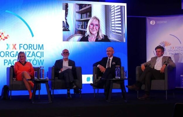 Uczestnicy forum siedzący w fotelach podczas dyskusji panelowej. Za nimi ekran z transmisją spotkania.