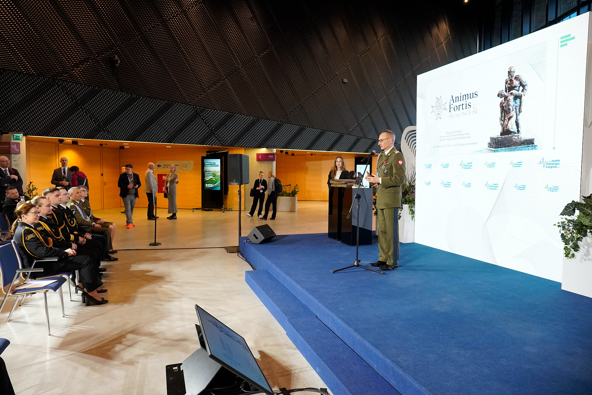 Dyrektor WIM Grzegorz Gielerak na scenie za nim wielki ekran z wyświetloną planszą Animus Fortis.