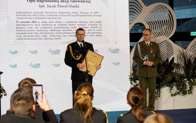 Jacek Paweł Osicki z dyplomem na scenie przemawia przy mikrofonie.