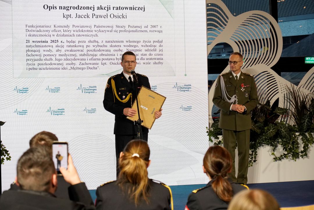 Jacek Paweł Osicki z dyplomem na scenie przemawia przy mikrofonie.