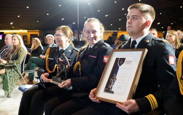 Przedstawiciele Akademii Pożarniczej z odebranym dyplomem siedzą wśród widowni.