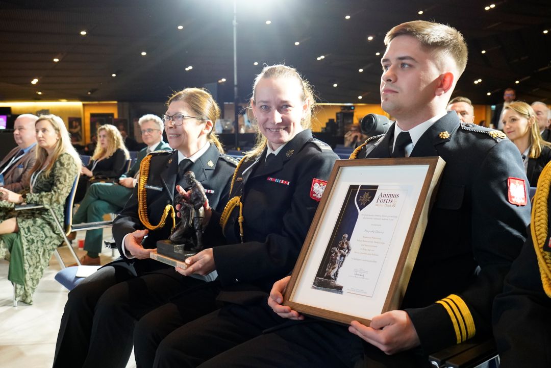 Przedstawiciele Akademii Pożarniczej z odebranym dyplomem siedzą wśród widowni.