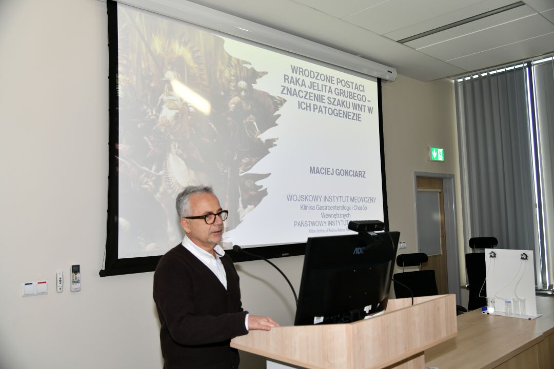 Maciej Gonciarz przy mównicy na sali WIM. Za nim wyświetlony slajd z prezentacji.