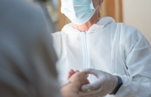 Lekarka w maseczce trzyma za dłoń osobę stojącą naprzeciw niej.