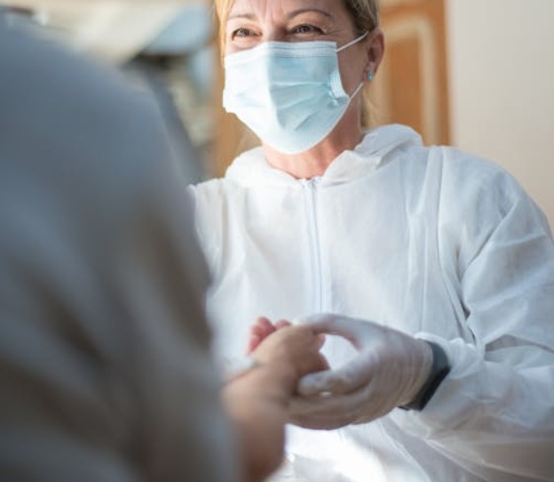 Lekarka w maseczce trzyma za dłoń osobę stojącą naprzeciw niej.