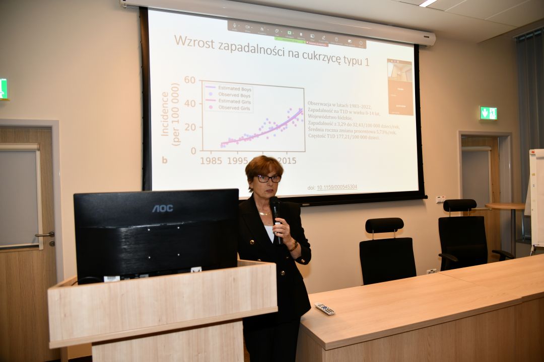 Agnieszka Szypowska z mikrofonem w ręku, podczas wykładu w sali LOMTI. Za nią tablica z prezentacją.