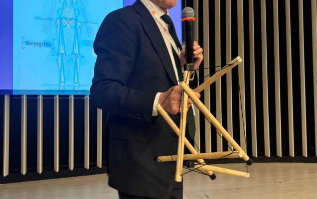 prelegent prowadzi prelekcję. Za nią wyświetlacz ze slajdem prezentacji.