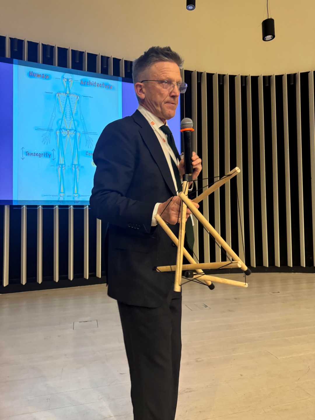 prelegent prowadzi prelekcję. Za nią wyświetlacz ze slajdem prezentacji.