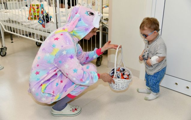 Zajączek wielkanocny z koszyczkiem ze słodyczami kuca przy małym pacjencie.