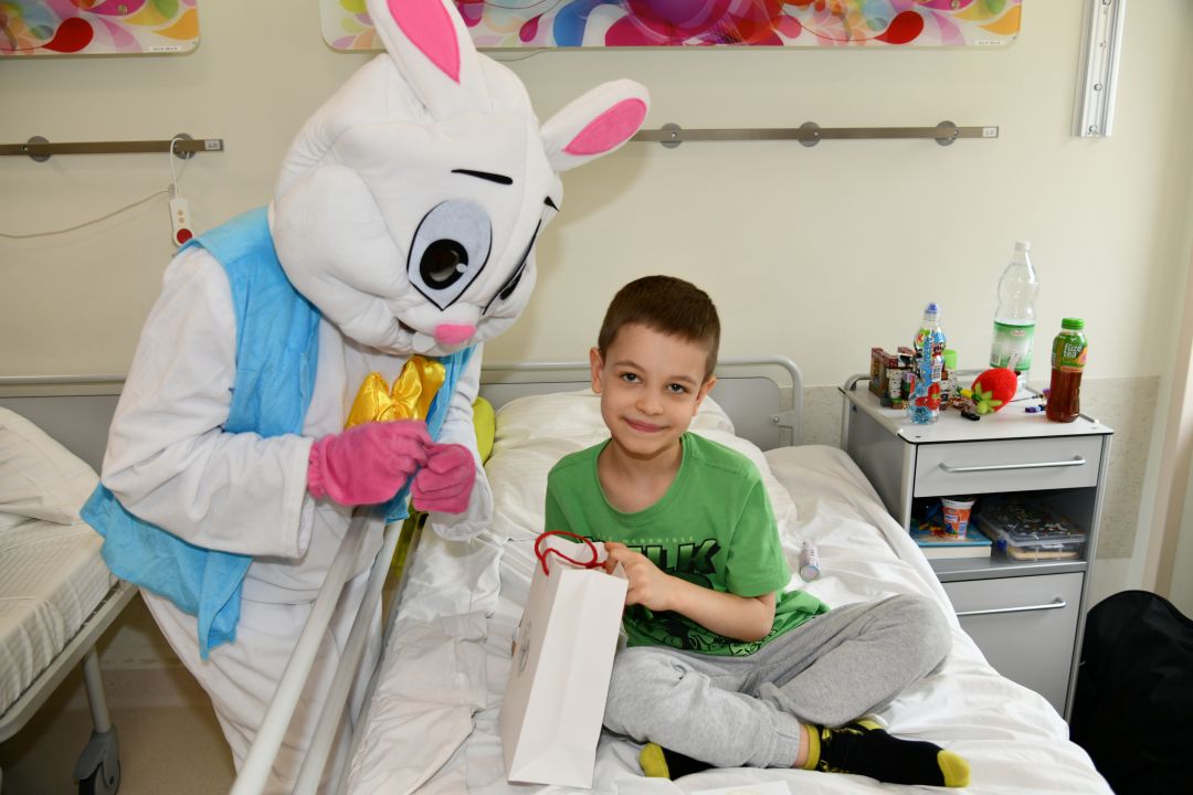 Zajączek wielkanocny w sali szpitalnej z młodym pacjentem siedzącym na łóżku trzymającym torbę z prezentem.