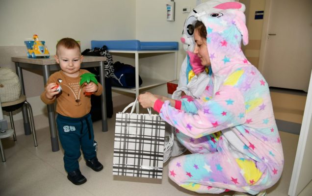 Zajączek wielkanocny w sali szpitalnej kuca przy małym chłopcu.