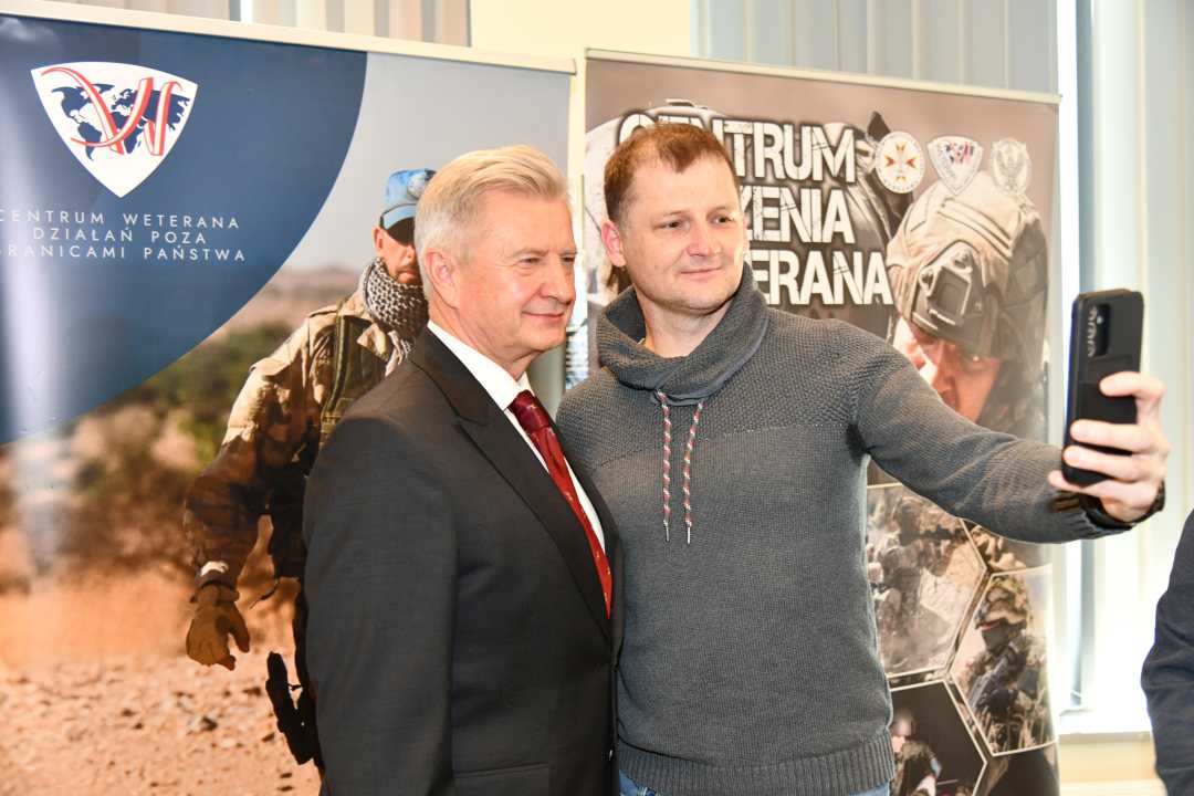 Uczestnik spotkania robi selfie z Stanisławem Wziątkiem na tle ścianki Centrum Leczenia Weterana.