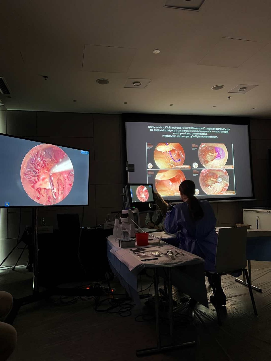 Przyciemniona sala. Przy stole laboratoryjnym siedzi mężczyzna. Przed nim na dwóch ekranach widok preparatów mikroskopowych.