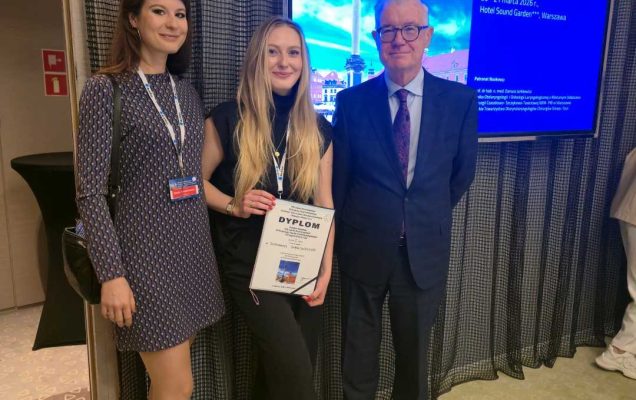 Dwie młode kobiety ze starszym mężczyzną. Jedna z kobiet trzyma w rękach dyplom. Za nimi ekran z wyświetloną prezentacją.