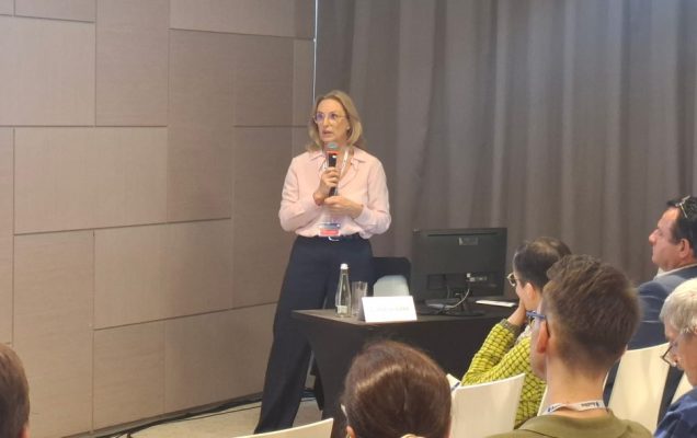 Prelegentka na scenie z mikrofonem w ręku.