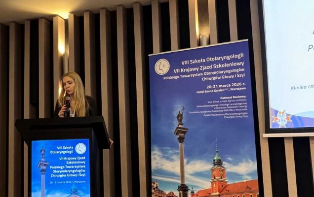 Prelegentka przy mównicy. Za jej plecami na ekranie wyświetlona prezentacja.