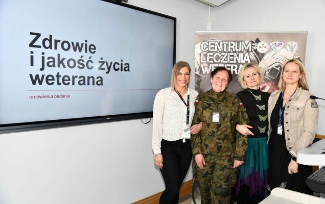 Barbara Betiuk, Marta Mnitowska, Marta Machunik, Karolina Wyczółkowska w sali wykładowej. Obok nich na ekranie slajd z prezentacji z napisem Zdrowie i jakość życia weterana. Za ich plecami ścianka reklamowa Centrum leczenia Weterana z żołnierzem podczas ćwiczeń na poligonie.