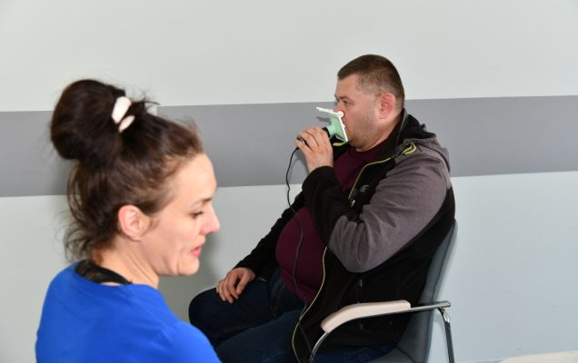 Lekarka wykonuje badanie spirometryczne siedzącemu naprzeciw niej mężczyźnie.